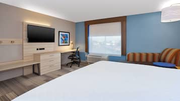Habitación de hotel con cama, escritorio con silla, televisor de pantalla plana, ventana con vistas y almohada estampada.