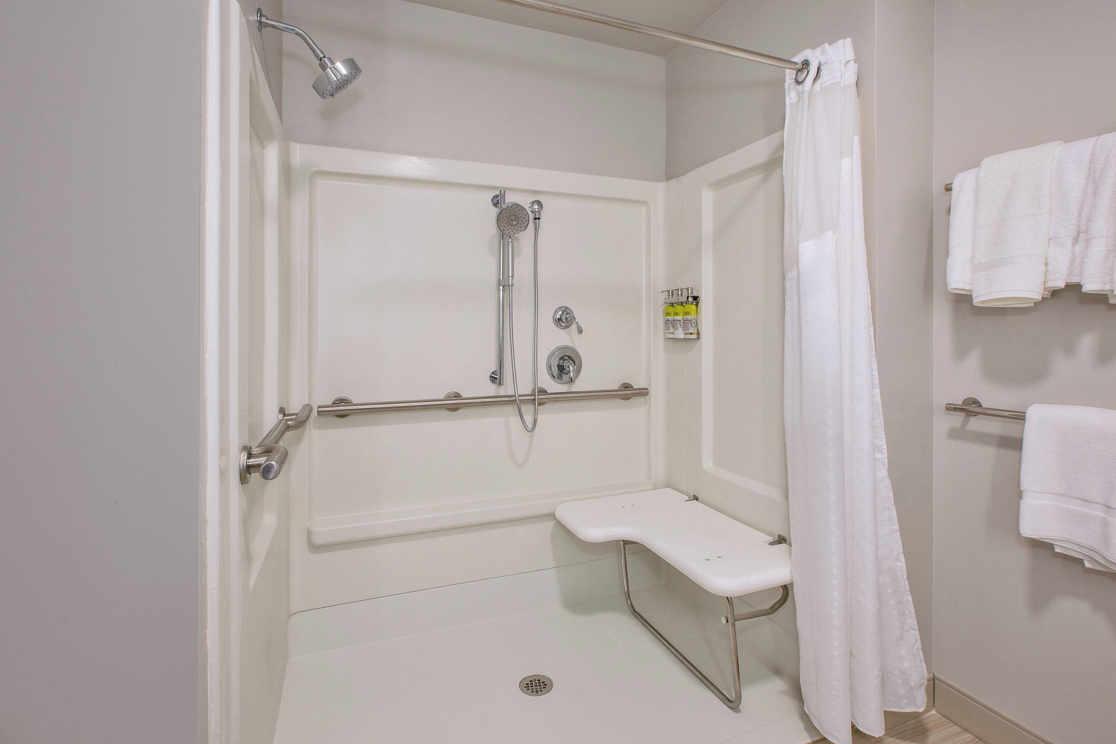 A bathroom with a shower, grab bar, bench, and towel rack.