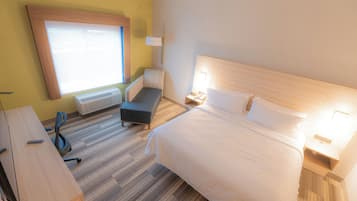 A hotel room with a bed, bedside table, lamp, and a window with blinds.