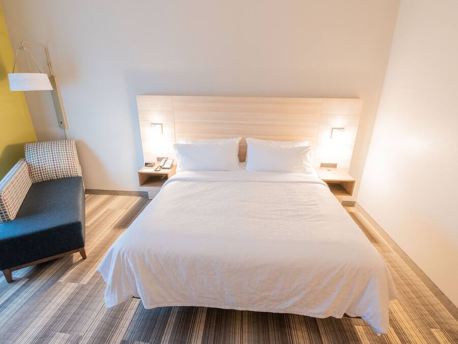 A neatly made bed with a wooden headboard, a bedside table with a lamp, and a patterned chair.