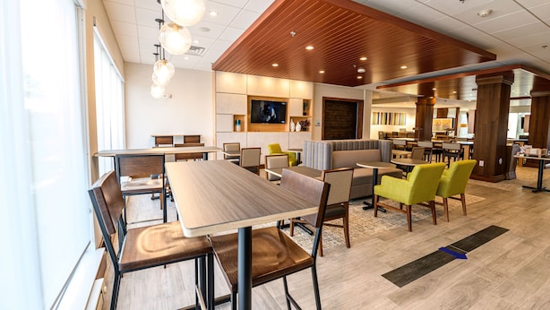 A modern hotel lobby with a wooden ceiling, a large TV screen, and a seating area with tables and chairs. - Holiday Inn Express & Suites Dayton East - Beavercreek by IHG (Dayton)