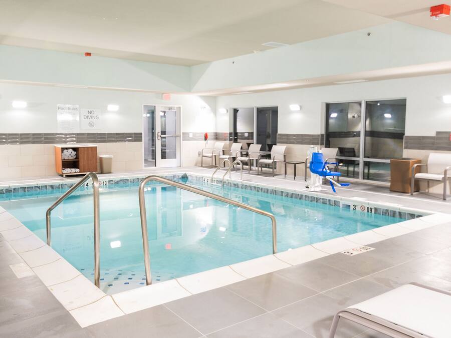 An indoor swimming pool with clear pool rules and no diving signs, surrounded by seating areas and a tiled floor.