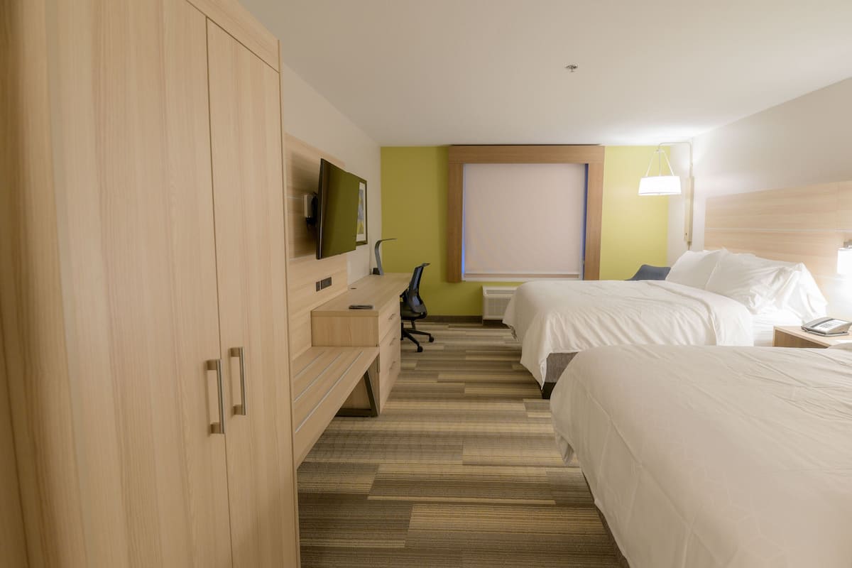 Ein Hotelzimmer mit zwei Betten, einem Schreibtisch mit Stuhl, einem Fernseher und einem großen Fenster.