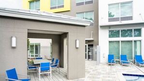 An outdoor pool area with blue chairs and a table, surrounded by a building with large windows and a tiled floor. - Holiday Inn Express Doral Miami by IHG (Miami)
