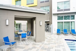 An outdoor pool area with blue chairs and a table, surrounded by a building with large windows and a tiled floor. - Holiday Inn Express Doral Miami by IHG (Miami)