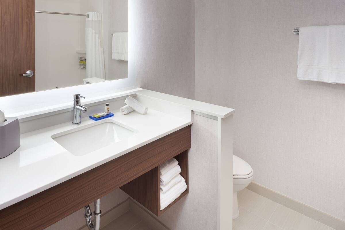 A modern bathroom with a white sink, a mirror, a towel rack, and a toilet.