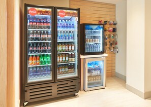 A vending machine area with multiple beverage dispensers, including Coca-Cola and other brands, and a small refrigerator. - Holiday Inn Express Doral Miami by IHG (Miami)