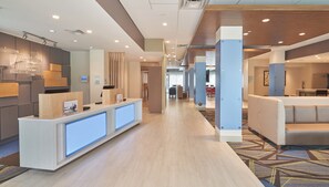 A hotel reception area with a reception desk, seating area, and a view into the dining space.