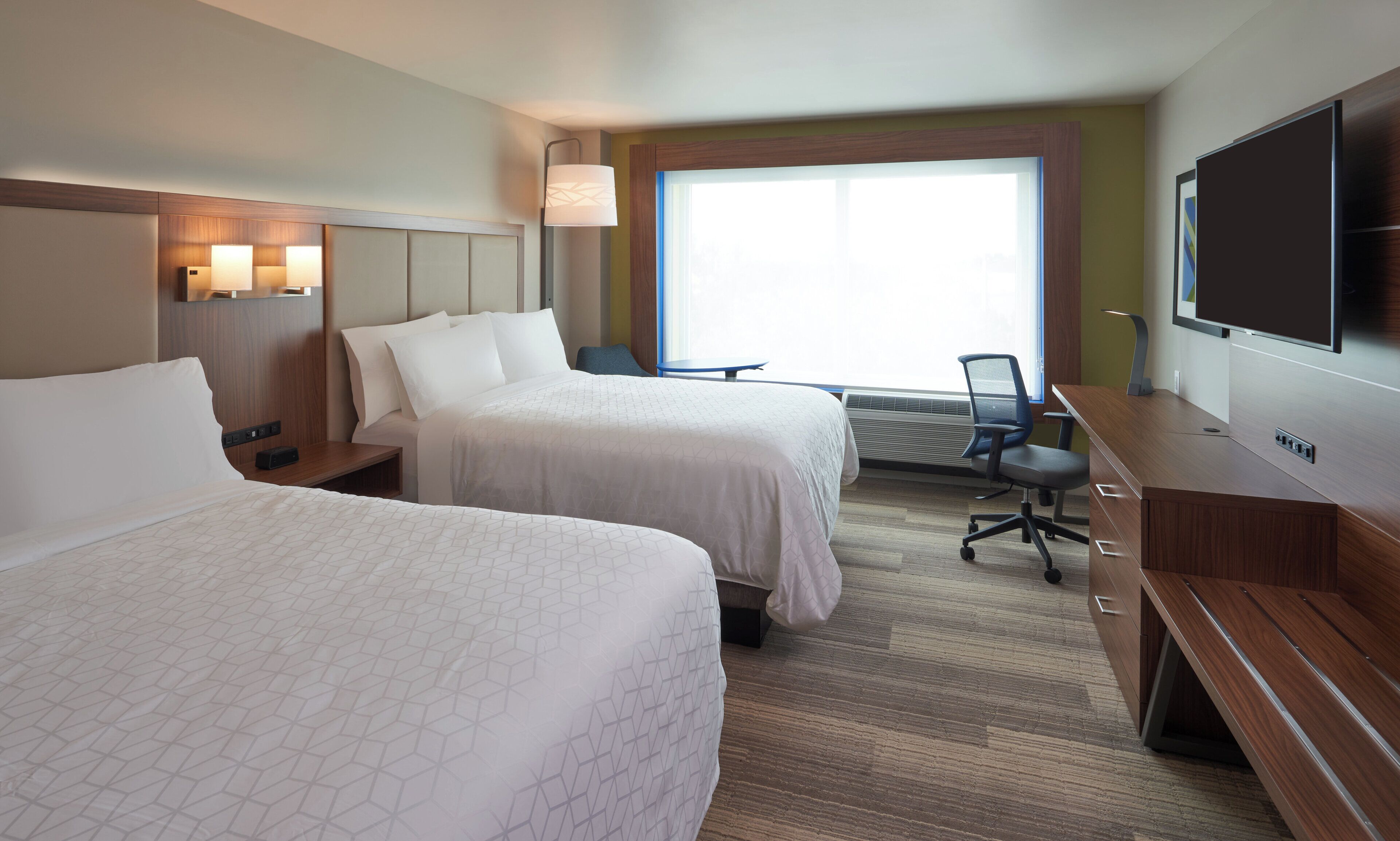 A hotel room with two beds, a desk, a chair, a television, and a window with blinds.