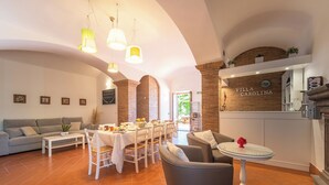 Amplia sala de estar con mesa de comedor, sofás y zona de cocina. Se lee un cartel con la inscripción 'Villa Carolina'.