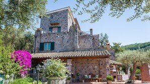 Un edificio de piedra con techo de tejas, balcón y jardín con flores y plantas.