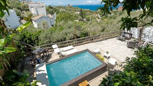 Una piscina en la azotea con vista al mar, rodeada de vegetación y edificios.