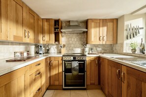 A kitchen with wooden cabinets, a stove, oven, and a knife rack. - Darly Cottage (Cheltenham)