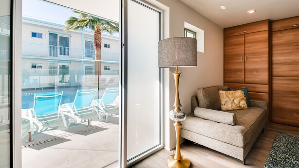 A modern living room with a large sliding glass door leading to a pool area, a sofa with cushions, and a tall floor lamp. - Hollywood Studios in Downtown Phoenix (Phoenix)
