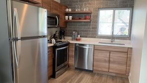 A modern kitchen with stainless steel appliances, wooden cabinets, a brick backsplash, and a window providing natural light. - Hollywood Studios in Downtown Phoenix (Phoenix)