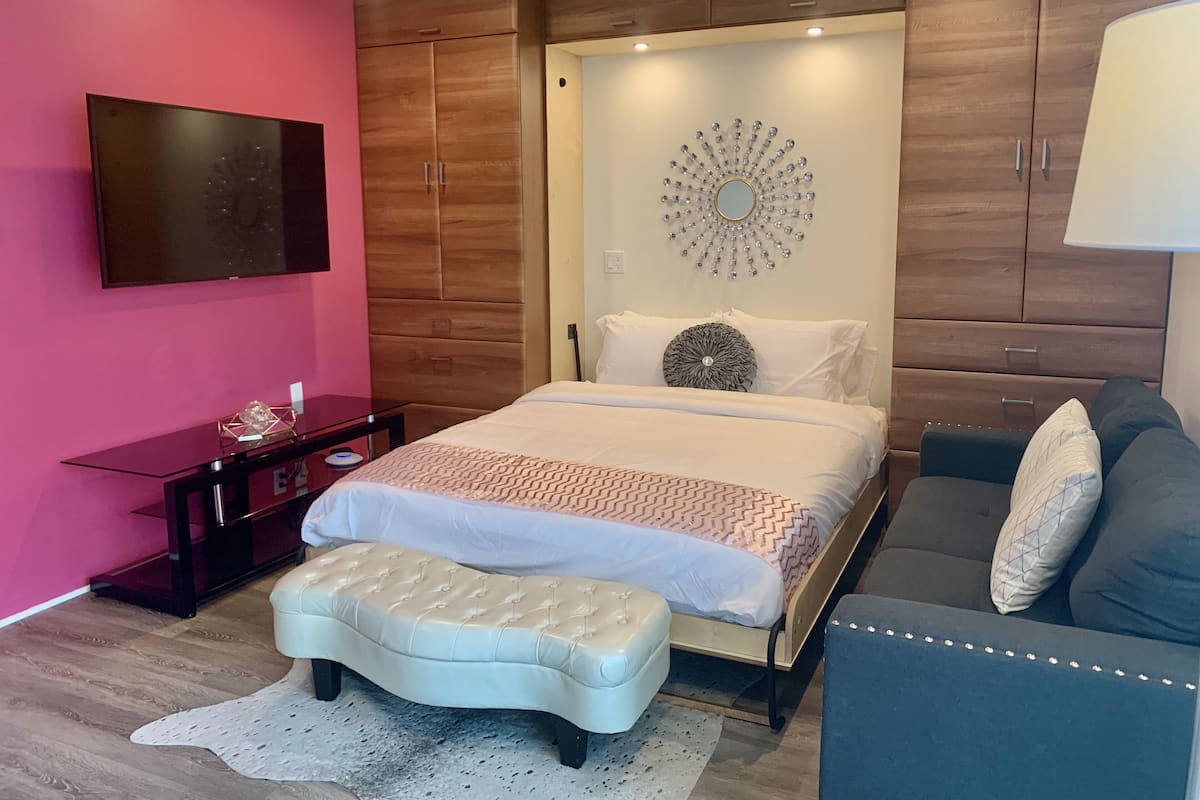 Une chambre à coucher moderne comprenant un lit, une table de chevet, une commode, un téléviseur et un élément décoratif mural.