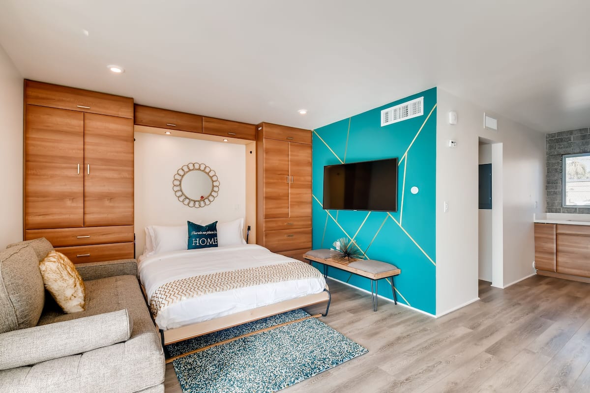 Une chambre moderne avec un lit, un canapé, une télévision et une armoire en bois.