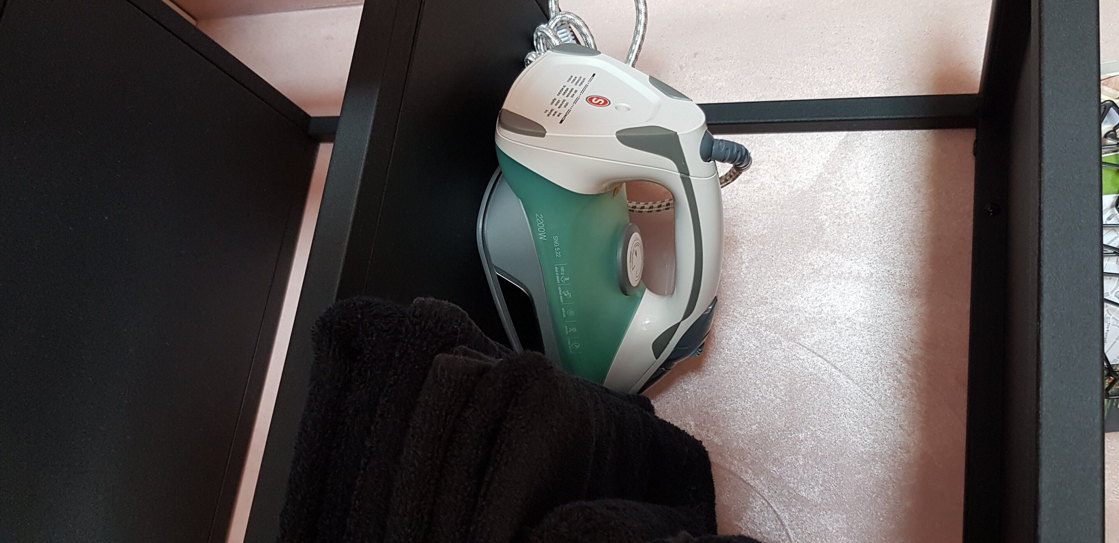 A green and white iron on a tiled floor.