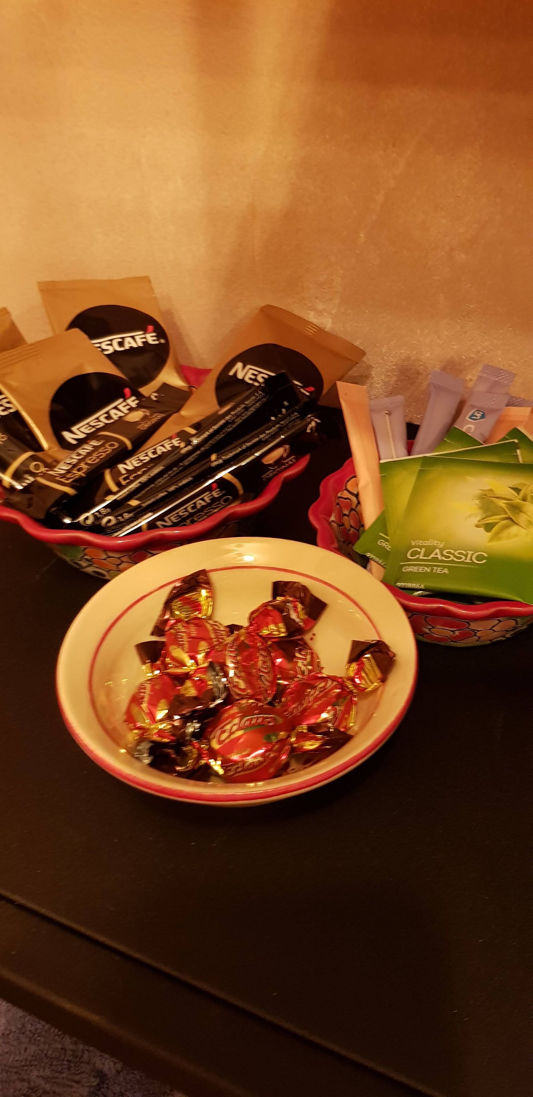 Un tazón con caramelos variados, un set de cápsulas de café Nescafé y un paquete de té verde clásico Vitality.