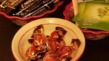 Un tazón con caramelos variados, un set de cápsulas de café Nescafé y un paquete de té verde clásico Vitality.