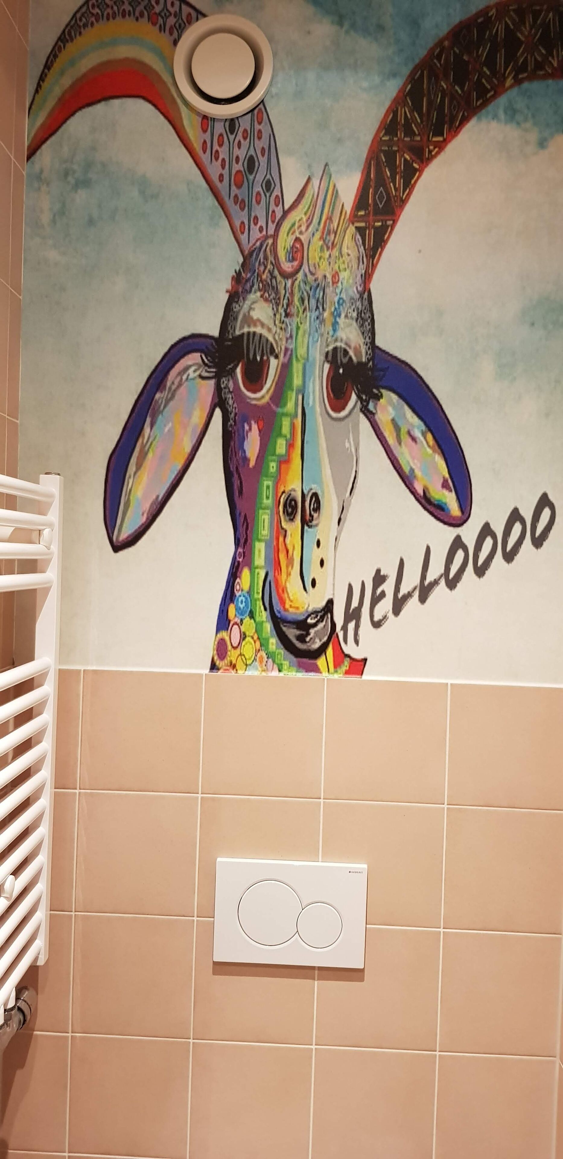 Une salle de bain ornée d’une fresque colorée représentant une girafe, et sur laquelle on peut lire le mot « HELLO ».
