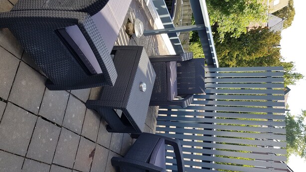 Mobilier d’extérieur pour patio, comprenant une table et des chaises en métal, une clôture blanche en bois et un sol pavé.
