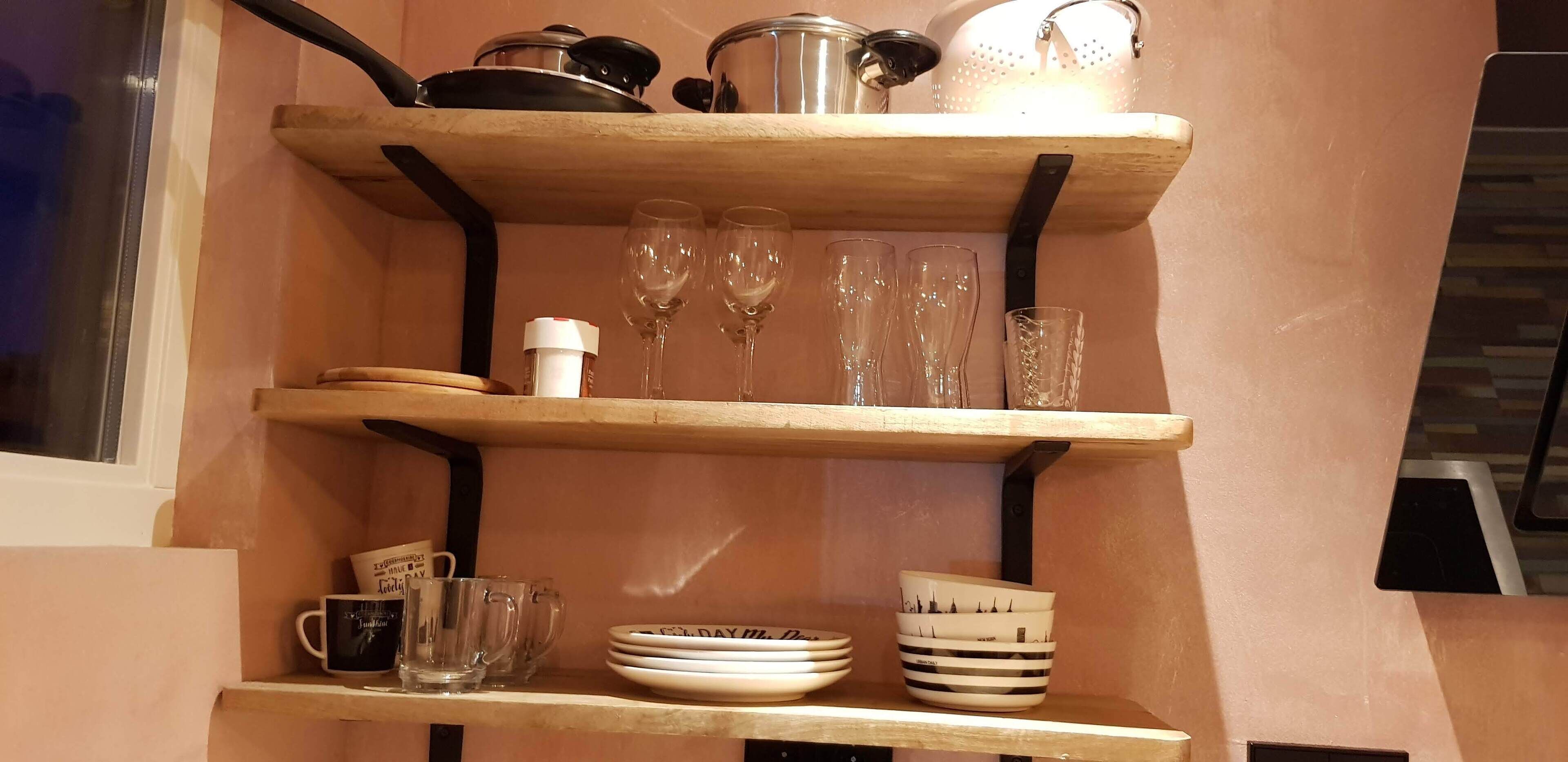 A kitchen shelf with various items including glassware, plates, and a mug.