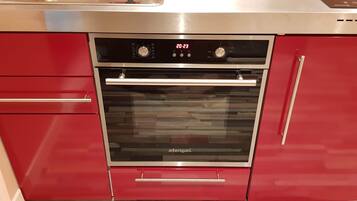 Ein einbaufertiger, edelstahlfarbener Backofen mit digitaler Anzeige, integriert in rote Schränke mit Schiebetür.