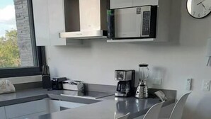 A modern kitchen with a central island, white chairs, and a coffee maker. - LUXURY APARTMENT IN KAAN HA, BAHIA PRINCIPE (Akumal)
