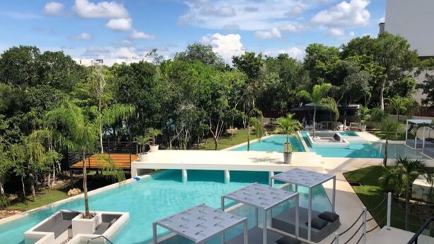 A pool area with multiple pools, lounge chairs, and a deck with a railing. - LUXURY APARTMENT IN KAAN HA, BAHIA PRINCIPE (Akumal)