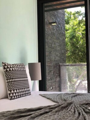 Experience serenity in this tranquil retreat with a large window offering a view of lush greenery and a neatly made bed.