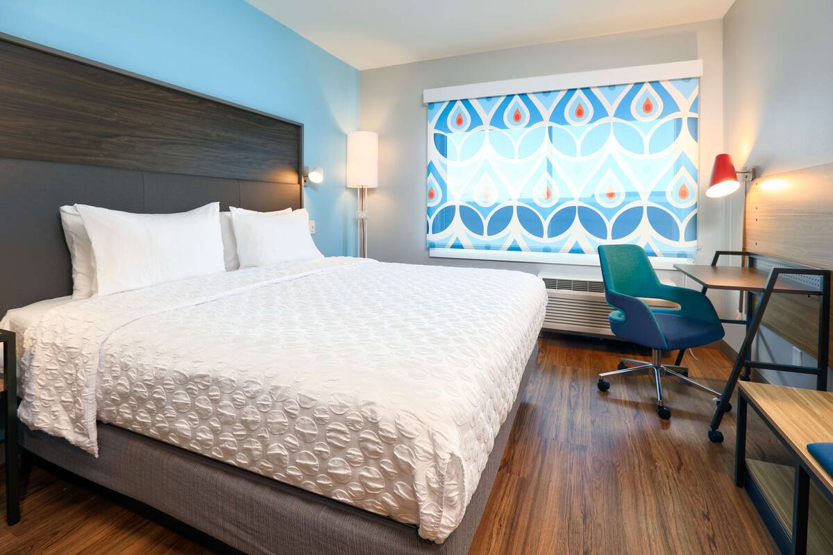 A hotel room with a large bed, a desk, a chair, and a window with a patterned view.