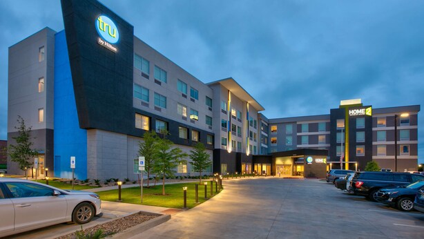 Un hotel moderno con un llamativo letrero de Tru by Hilton, varios espacios de estacionamiento y un área de entrada bien iluminada.