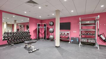 Ein Fitnessraum mit rosafarbenen Wänden, Trainingsgeräten und einer Spiegelwand.