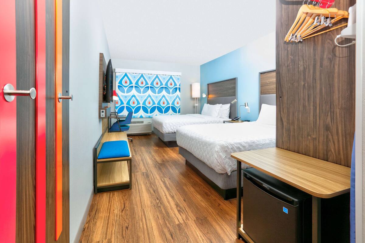 A hotel room with a bed, a desk, a chair, a small refrigerator, and a TV.