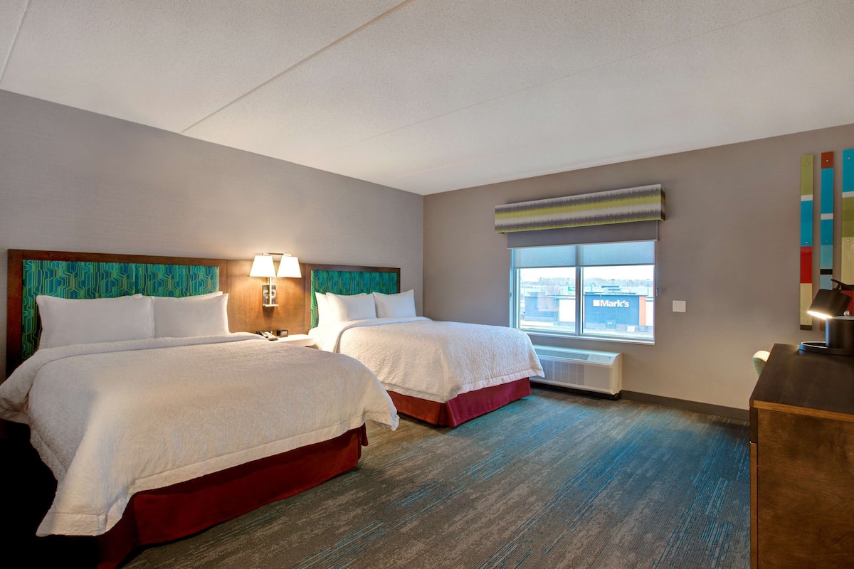 Ein Hotelzimmer mit zwei Betten, einem Fenster mit Stadtblick, einem Schreibtisch und einer Lampe.