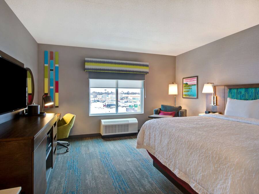 Habitación de hotel con una cama grande, un escritorio con televisión de pantalla plana, una silla, una ventana con vistas y aire acondicionado de pared.
