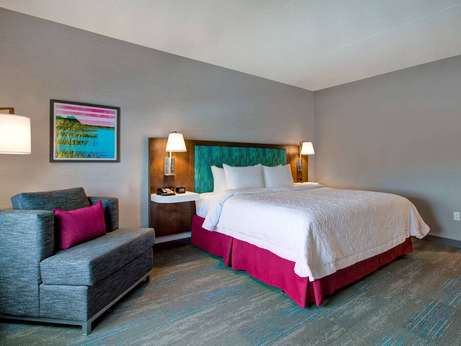 Una habitación de hotel con cama, sofá, mesita de noche y lámpara de pared.