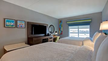 A hotel room with two beds, a TV, a desk, and a window with a view.