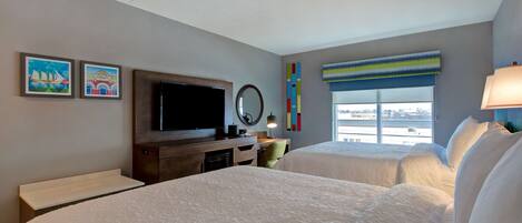 A hotel room with two beds, a TV, a desk, and a window with a view.
