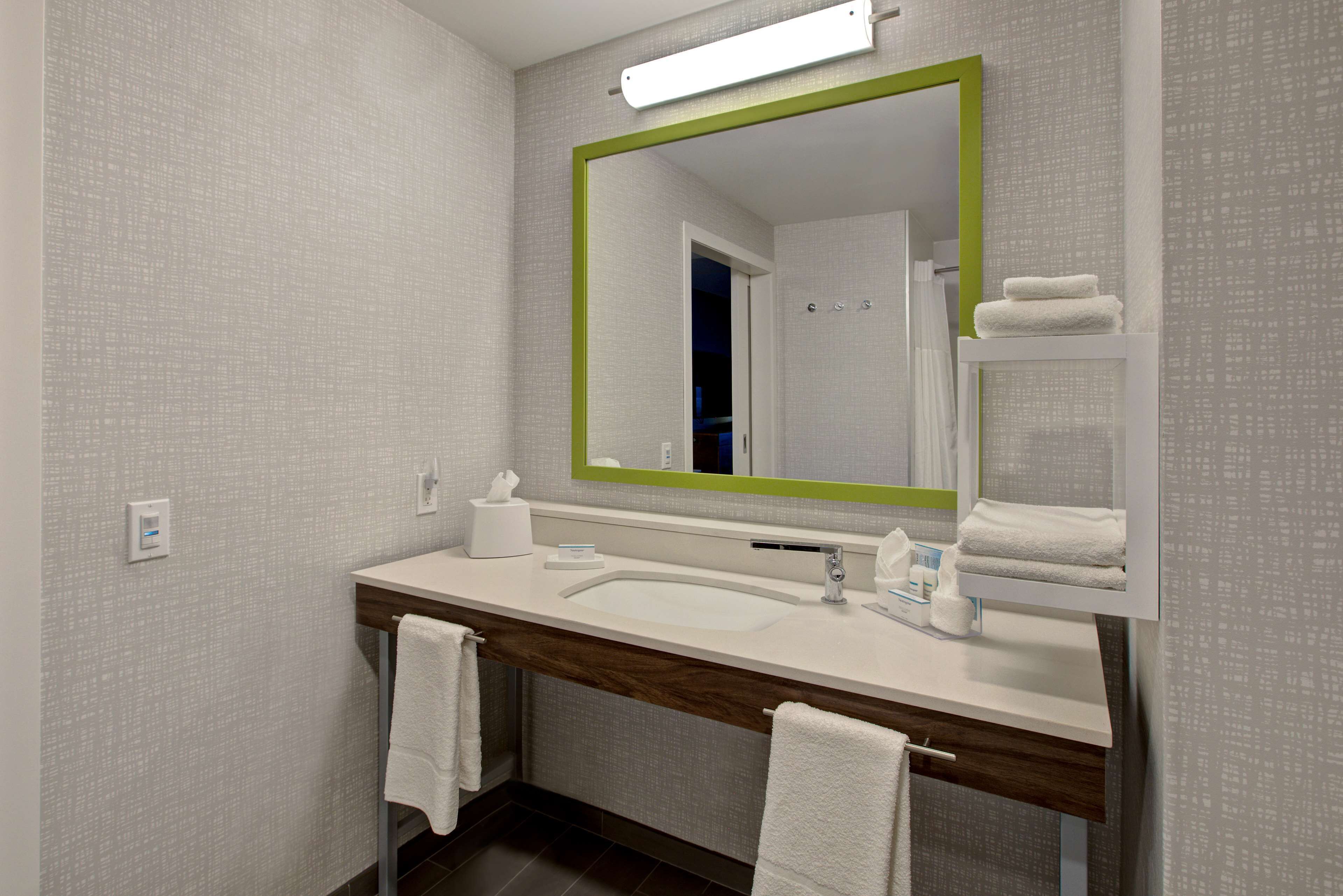 Un baño moderno con un espejo grande, lavamanos blanco y dos toallas colgadas en la pared.