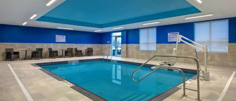 Ein Hallenschwimmbad mit deutlich markierten Bahnen, einem Rettungsschwimmerstuhl und einer Sitzgelegenheit am Beckenrand.