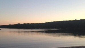 A calm lake at dusk with kayaks and a tent on the shore. - Lake Front Cottage Right Across Street ORV And Snowmobile, Blue Bear trail (Mancelona)