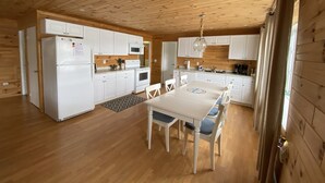 A compact kitchen with white cabinets, a refrigerator, a microwave, and a stove. There is a dining table with chairs and a rug. - Lake Front Cottage Right Across Street ORV And Snowmobile, Blue Bear trail (Mancelona)