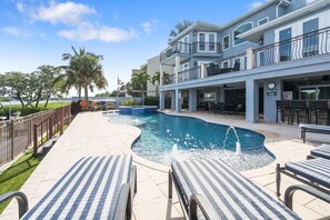 Un espace piscine avec des chaises longues, un élément décoratif aquatique et un bâtiment doté d’une terrasse.