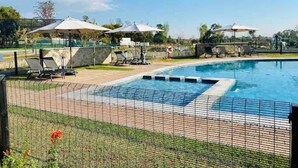 A swimming pool with a tiled deck, surrounded by lounge chairs and umbrellas. - Bobo's Greenlee Lifestyle Studio Apartment (Sandton)