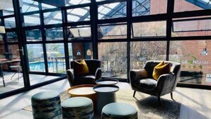 A modern interior with large windows, a seating area with armchairs and ottomans, and a visible pool outside. - Bobo's Greenlee Lifestyle Studio Apartment (Sandton)