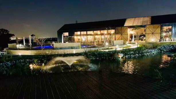 A modern building with a large glass facade, a wooden deck, and a water feature in front. - Bobo's Greenlee Lifestyle Studio Apartment (Sandton)