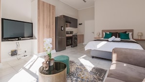 A modern hotel room with a bed, a TV, a kitchen area, and a bathroom. - Bobo's Greenlee Lifestyle Studio Apartment (Sandton)