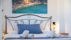 Una cama bien hecha con almohadas azules y toallas enrolladas, un cabecero de metal negro y un cuadro con una escena costera.